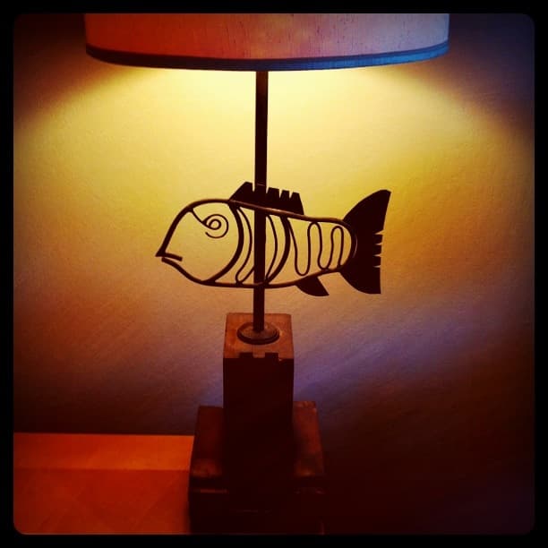 A wrought-iron fish lamp glowing warmly against a plaster wall.